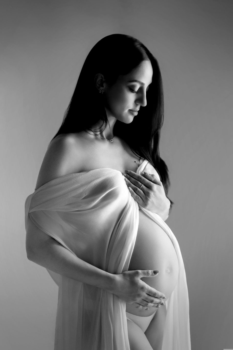 Maternité Femme enceinte, vêtue d'un drapé léger, caressant son ventre, en noir et blanc.
