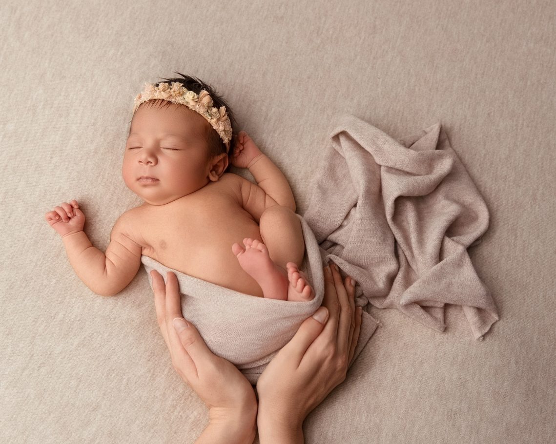 Naissance Bébé endormi enroulé dans un tissu, avec un diadème floral sur la tête.